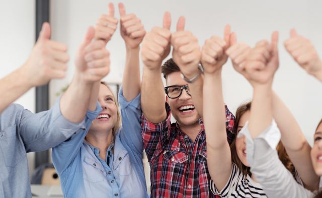 Erfolgreiches Team im Büro zeigt Daumen hoch
