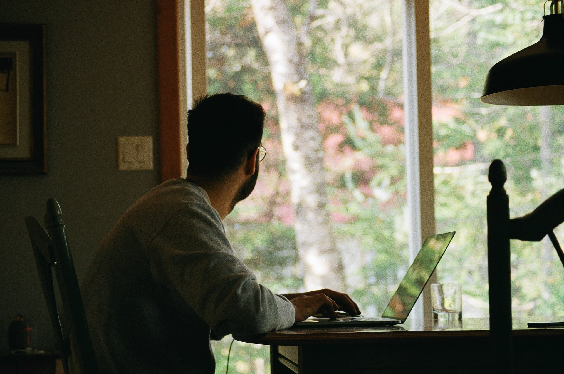 Ein Mann sitzt am Laptop und sieht aus dem Fenster