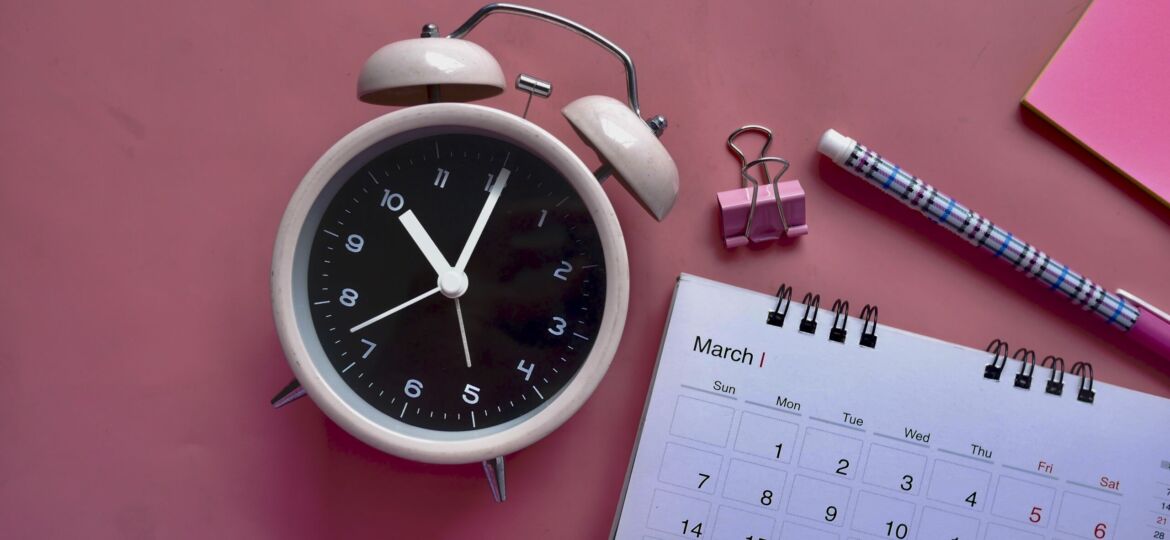 Ein Wecker steht neben einem Kalender