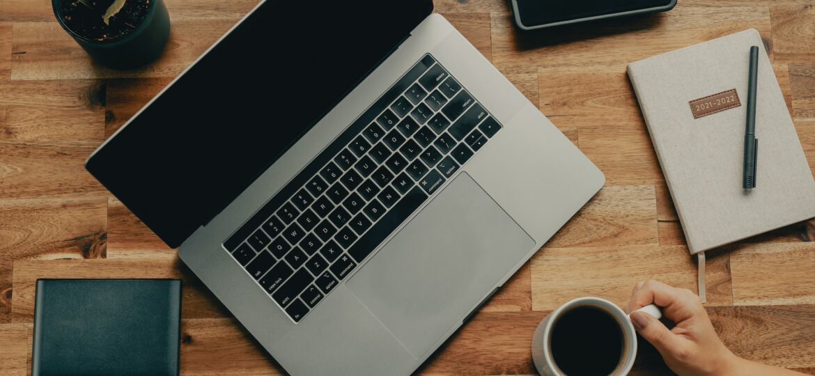 Ein Laptop, Handy, Notizblock und eine Kaffeetasse stehen auf einem Tisch