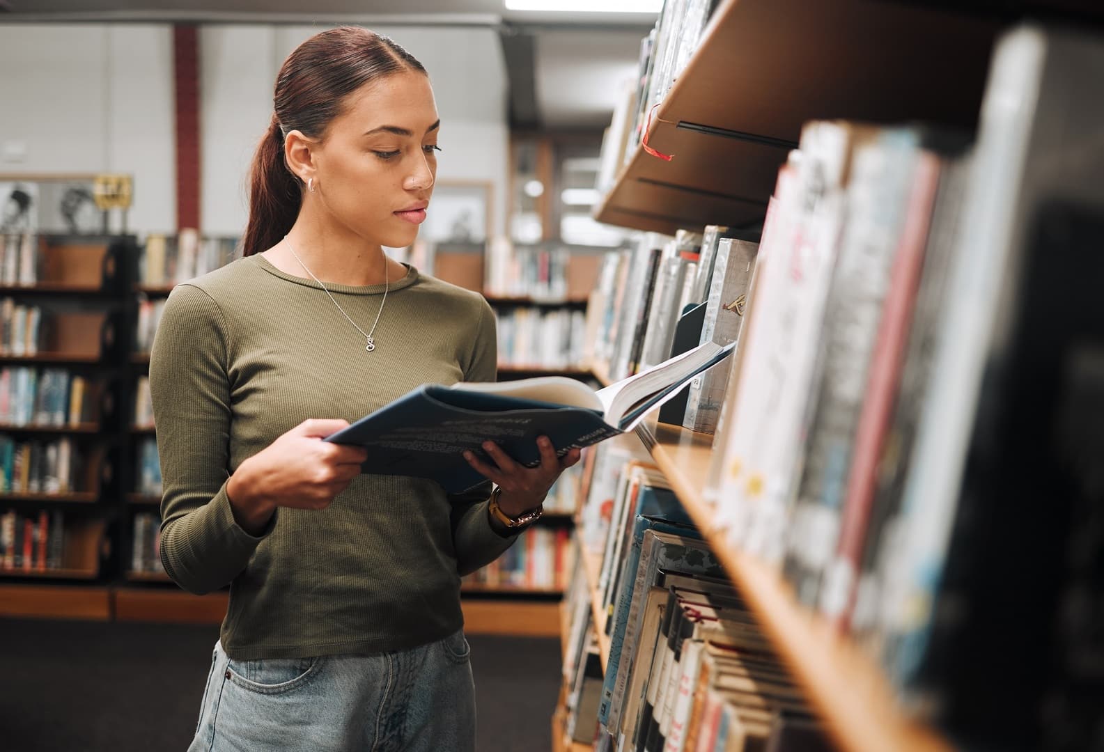 Eine Frau steht zwischen Bücherregalen und liest ein Buch