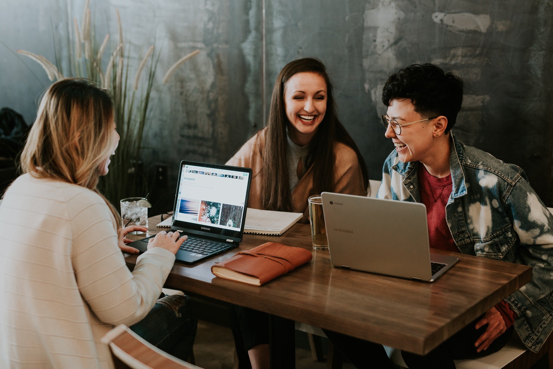 Drei Frauen sitzen vor ihren Laptops und lachen gemeinsam