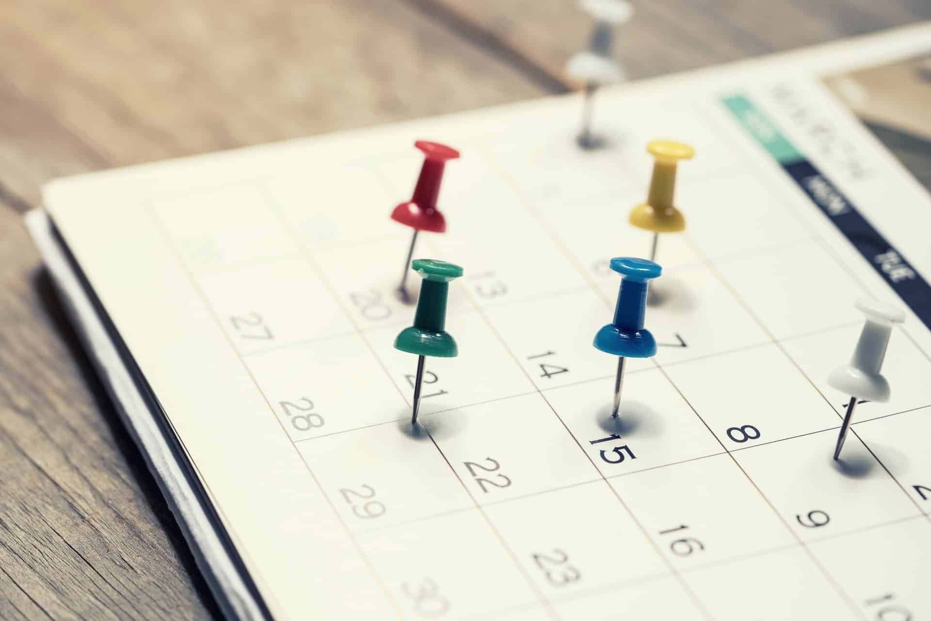 Bunte Pins im Kalender auf Holztisch