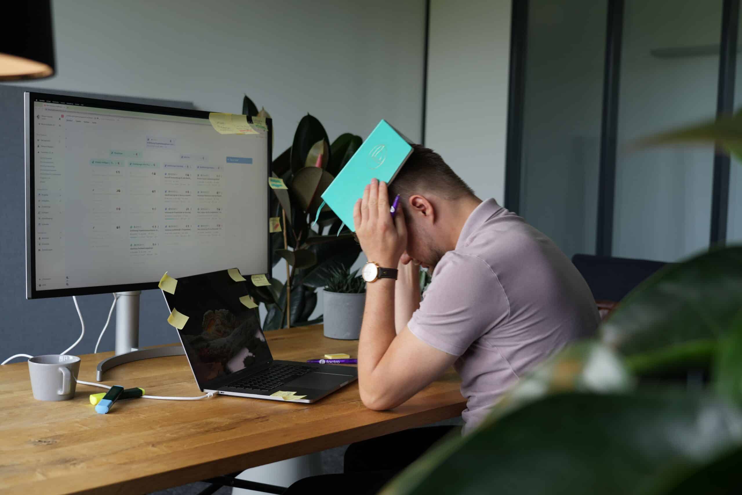 Ein Mann sitzt verzweifelt an einem mit Post-its übersäten Schreibtisch