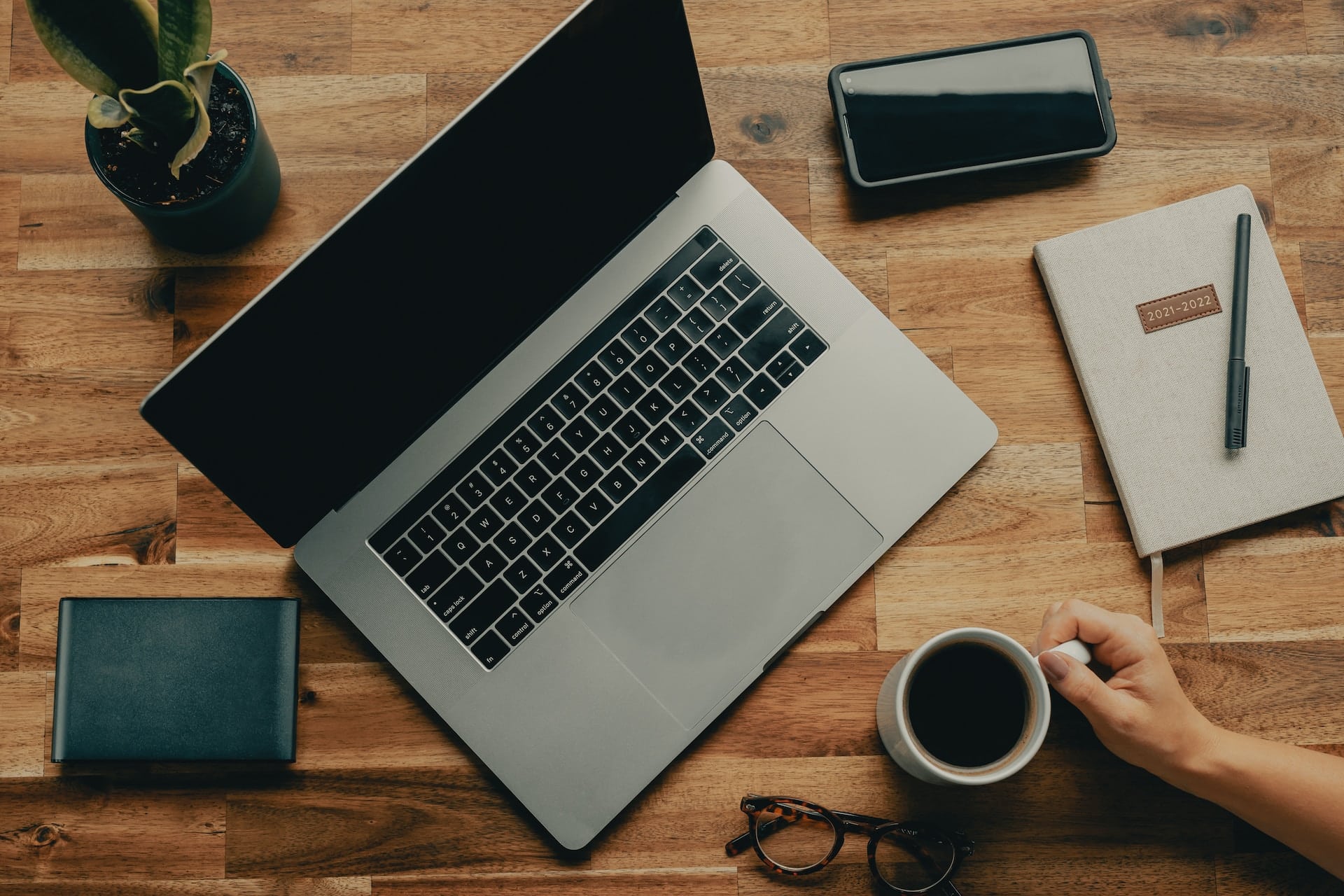 Ein Laptop, Handy, Notizblock und eine Kaffeetasse stehen auf einem Tisch