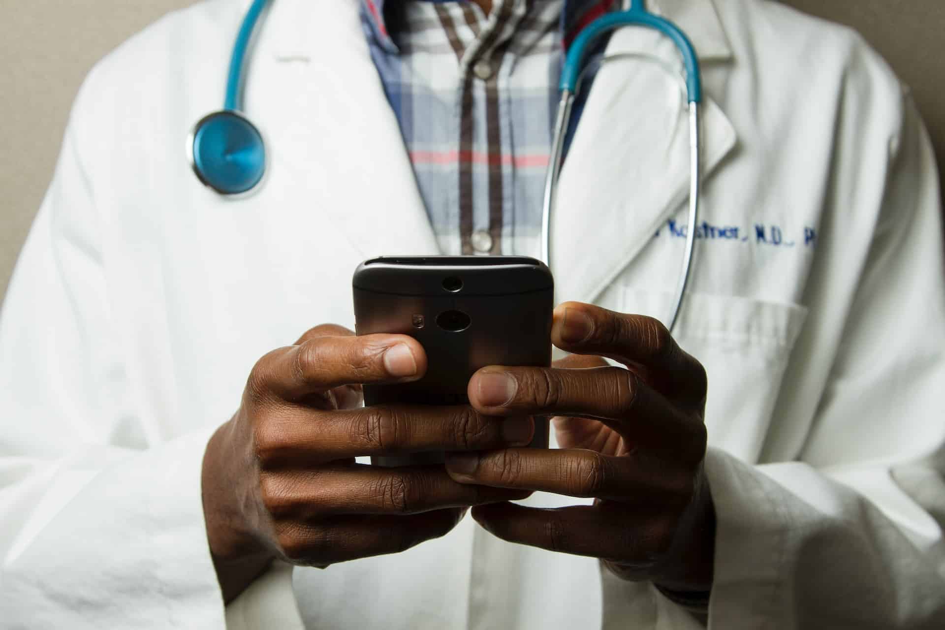 Eine Person mit Arztkittel hält ein Smartphone in der Hand