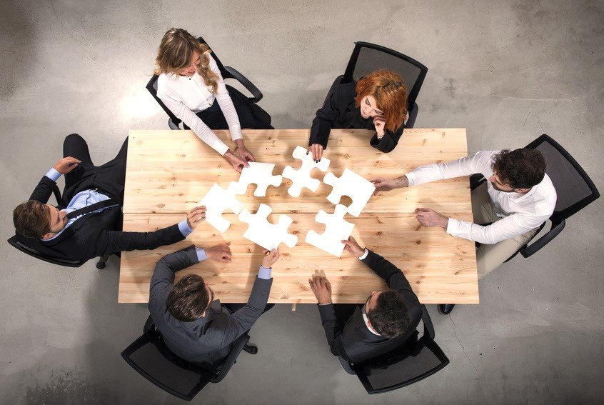 Ein Team setzt am Tisch einzelne Puzzlestücke zusammen