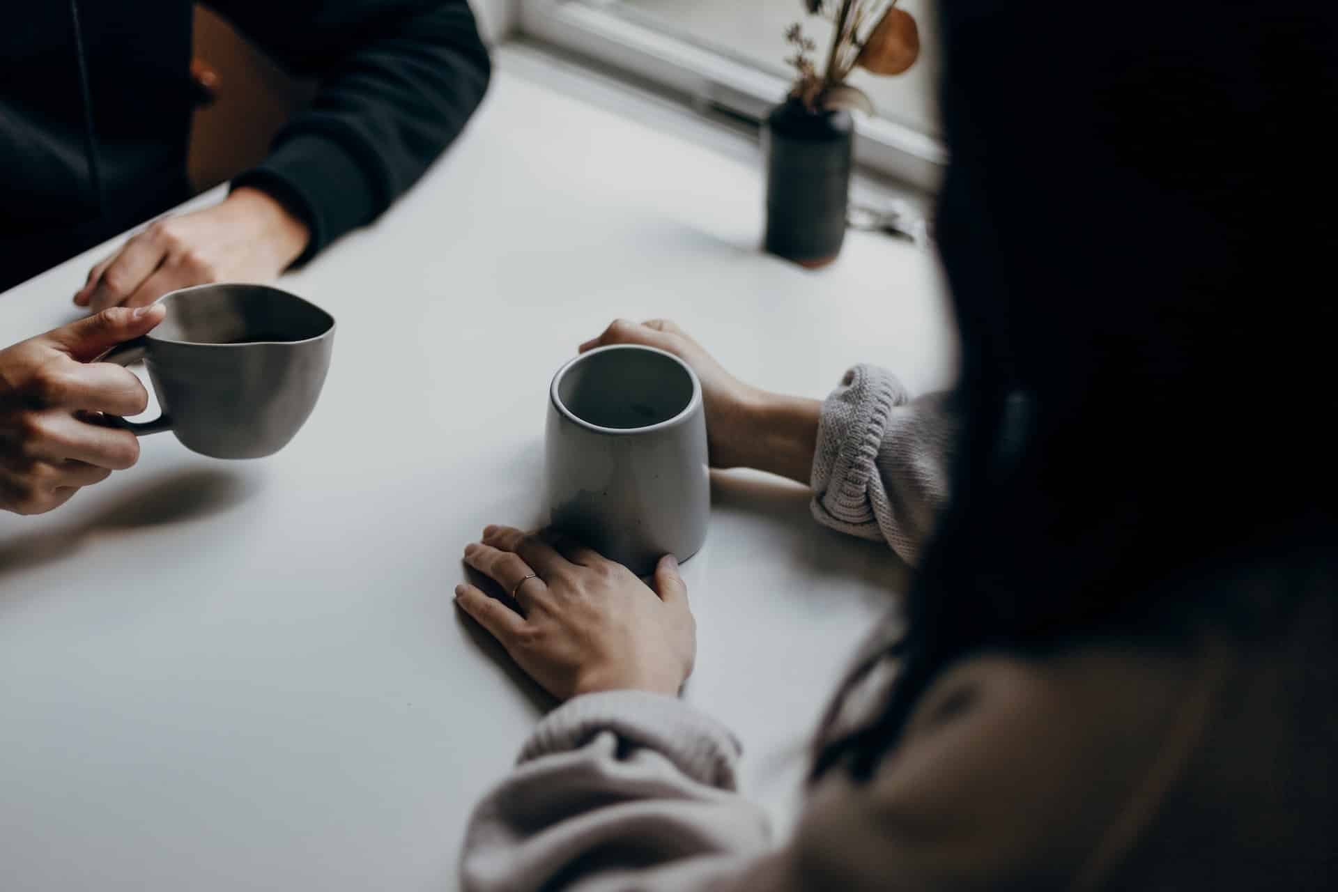 Zwei Personen sitzen an einem Tisch und halten Tassen in der Hand