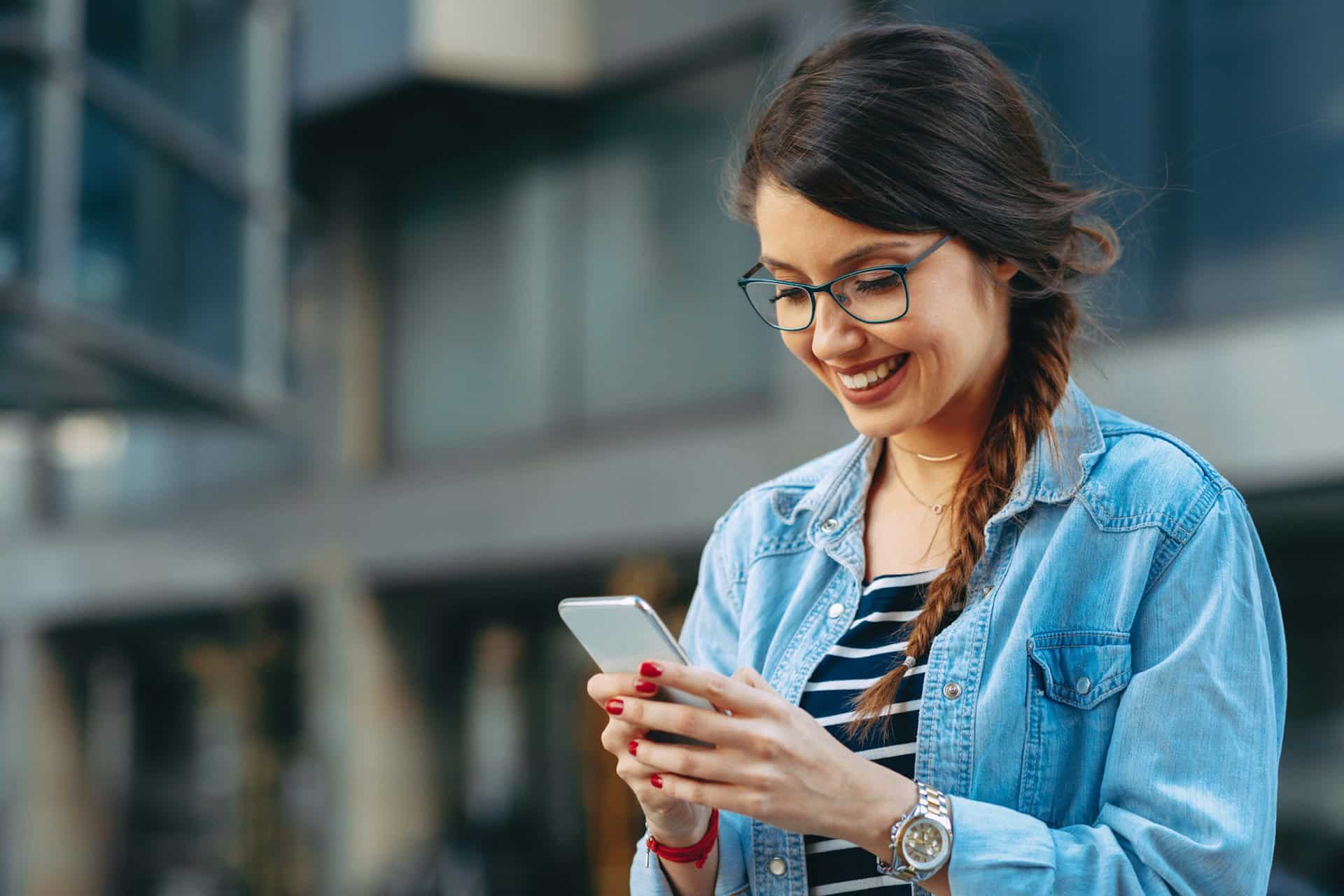 Junge Frau liest unterwegs eine Nachricht auf ihrem Smartphone