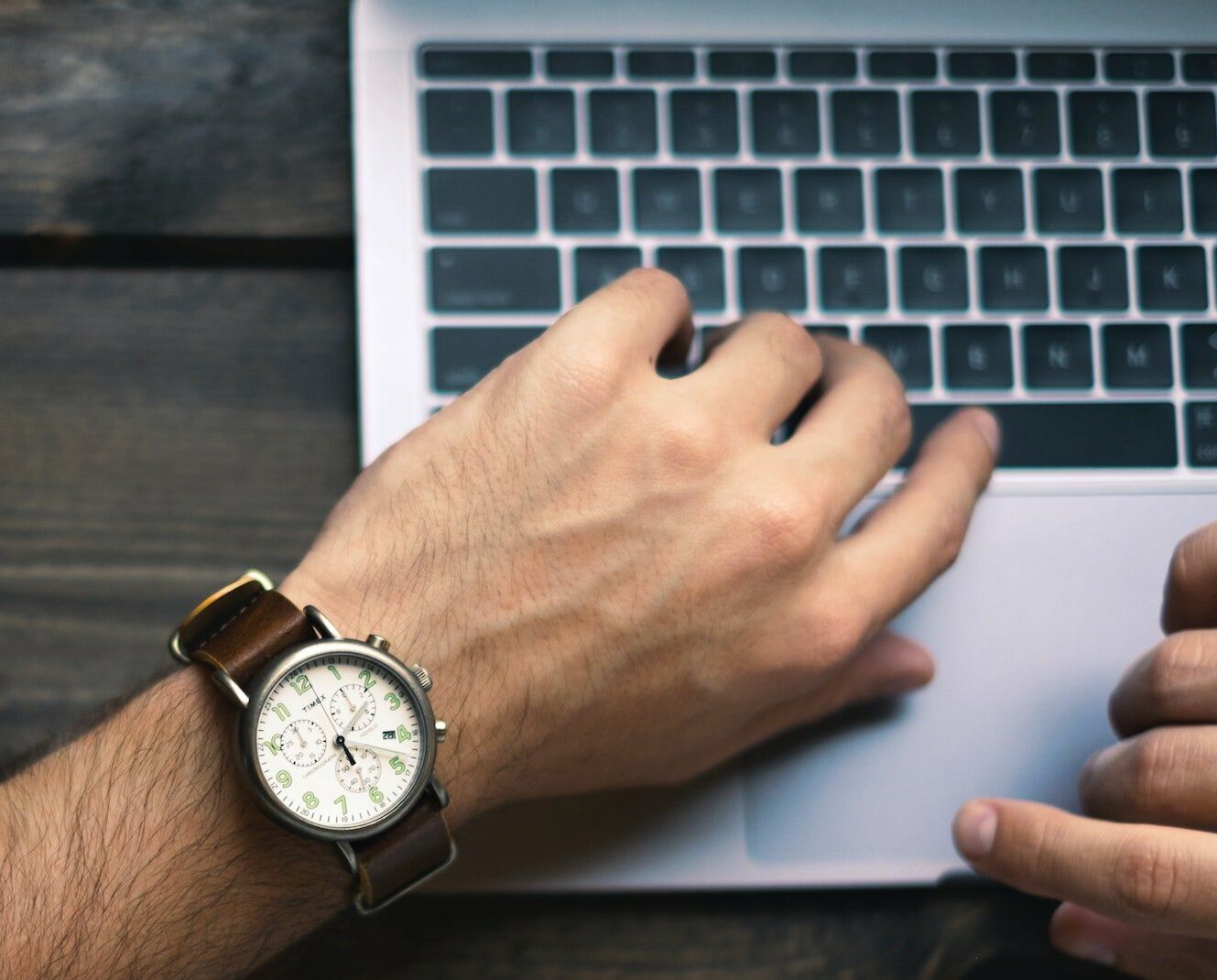 Ein junger Mann schaut am Laptop auf die Uhr