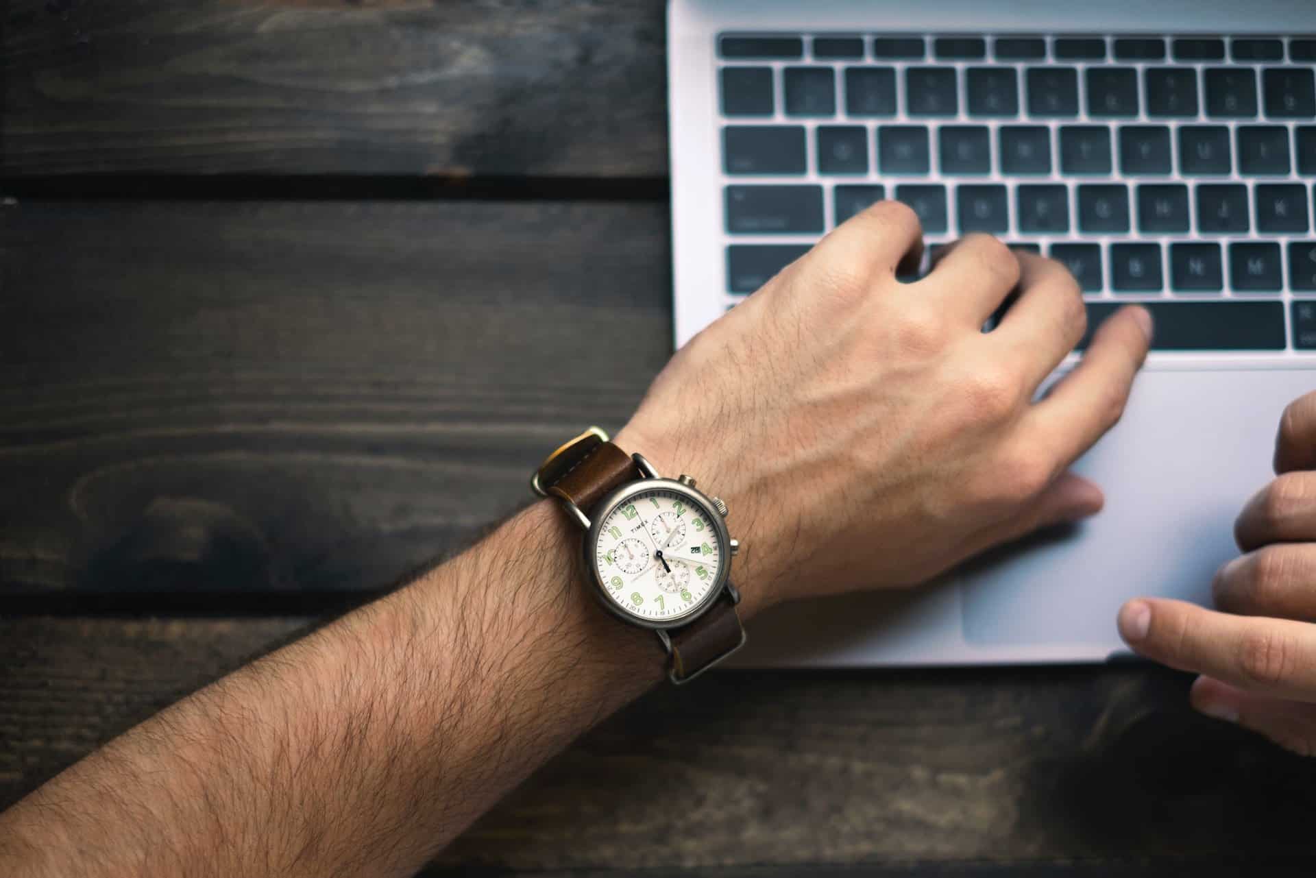 Ein junger Mann schaut am Laptop auf die Uhr