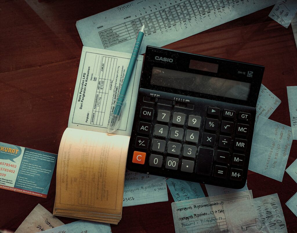 Earned Value Analyse: Definition, Berechnung & Umsetzung Auf einem Tisch liegt ein Taschenrechner und daneben ein Checkbuch. Auf dem Tisch verteilt liegen Rechnungen