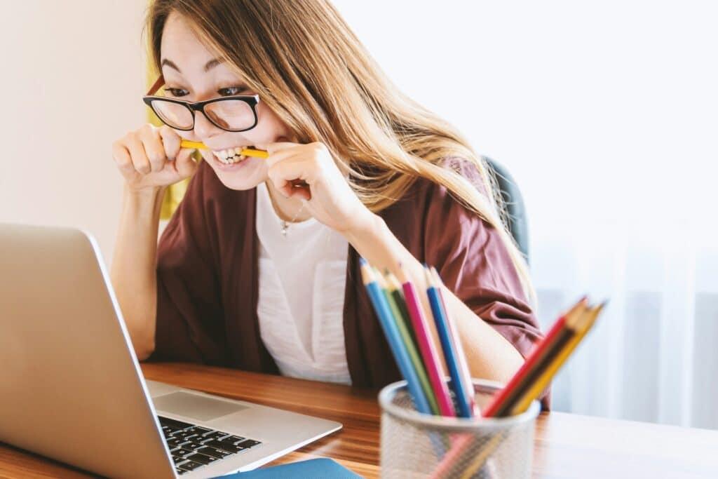 Scope Creep im Projektmanagement erkennen: Ursachen & Tipps Eine Frau sitzt vor einem Laptop und beißt frustriert auf einen Stift