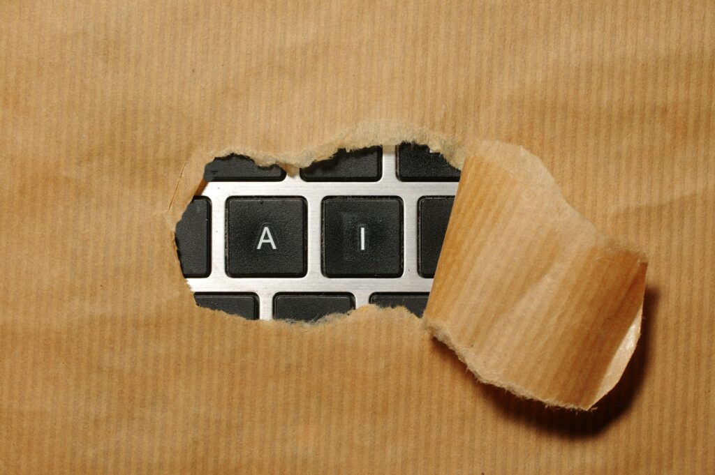 Eine Laptop-Tastatur ist mit braunem Papier abgedeckt, in der Mitte ist ein Loch, aus dem die Buchstaben A und I herausblitzen