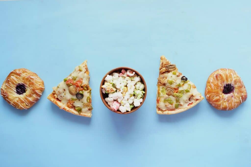 Eine ästhetisch angeordnete Auswahl an Snacks auf hellem Hintergrund: Pizza, Popcorn und süßes Gebäck.